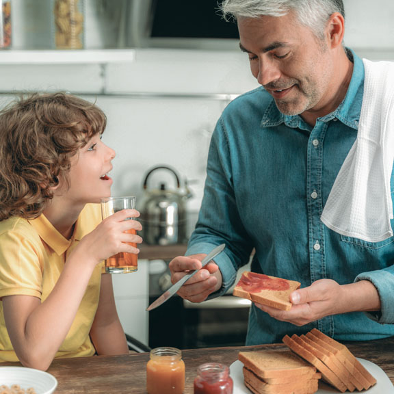 Smiling mature father making yummy breakfast with toast bread for little and happy son